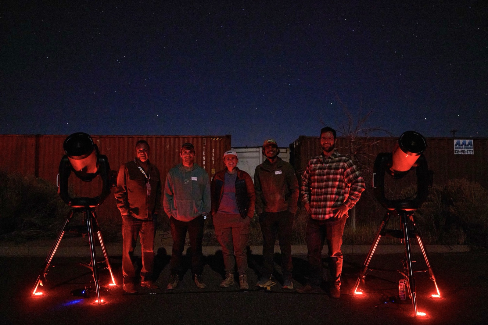 A group of people watching a stargazing presentation outdoors at night