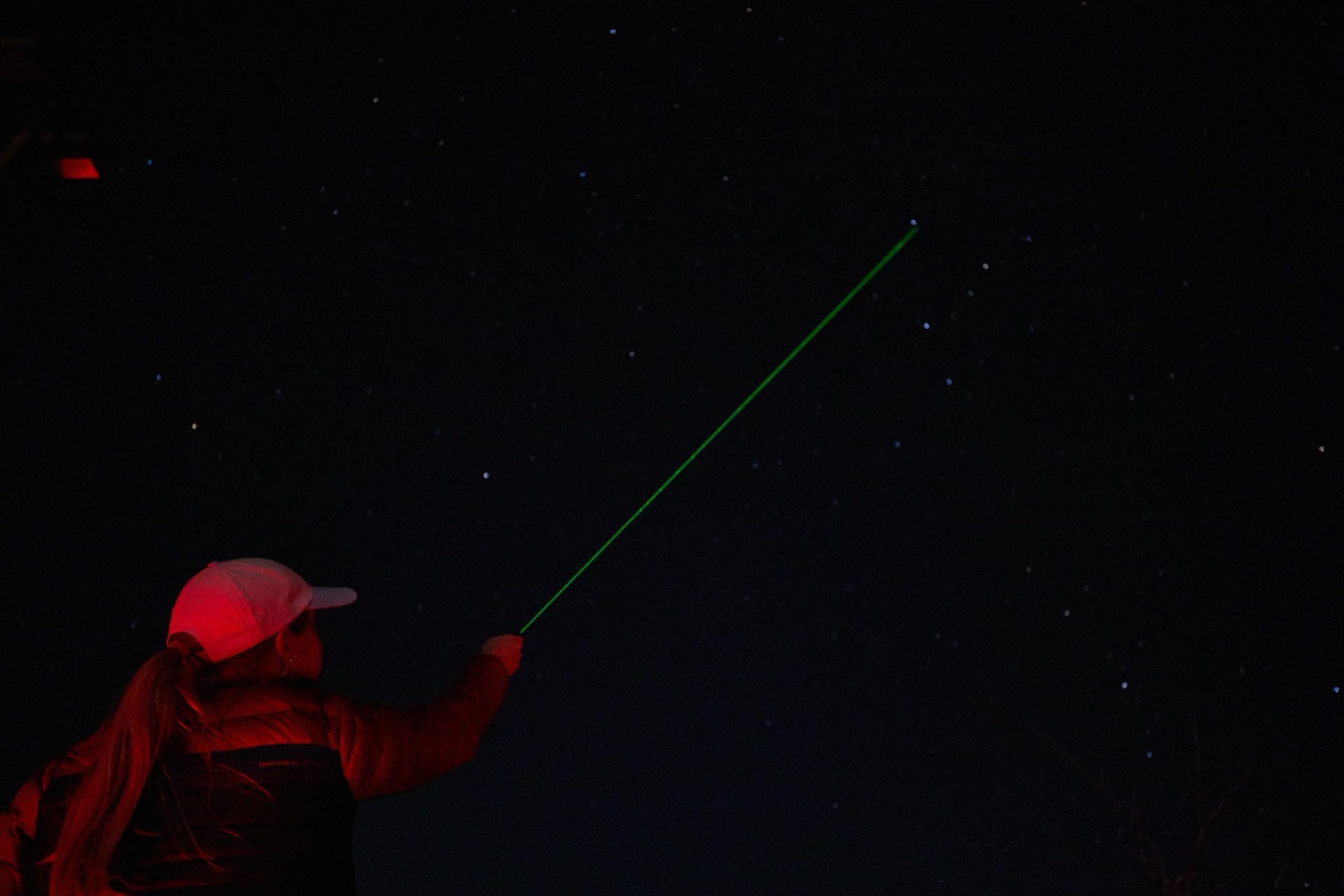 A guide pointing out constellations with a green laser under a starry sky