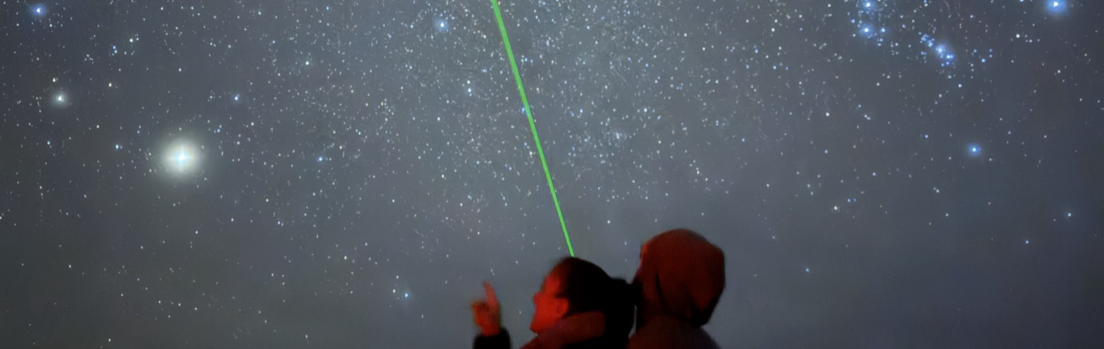 A wide shot of a tour group watching a guide point out stars with a laser pointer